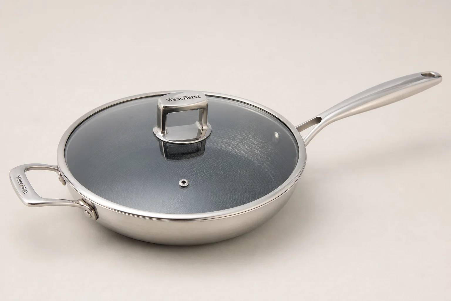 Collection of six stainless steel frying pans with varied finishes and handle styles on concrete surface