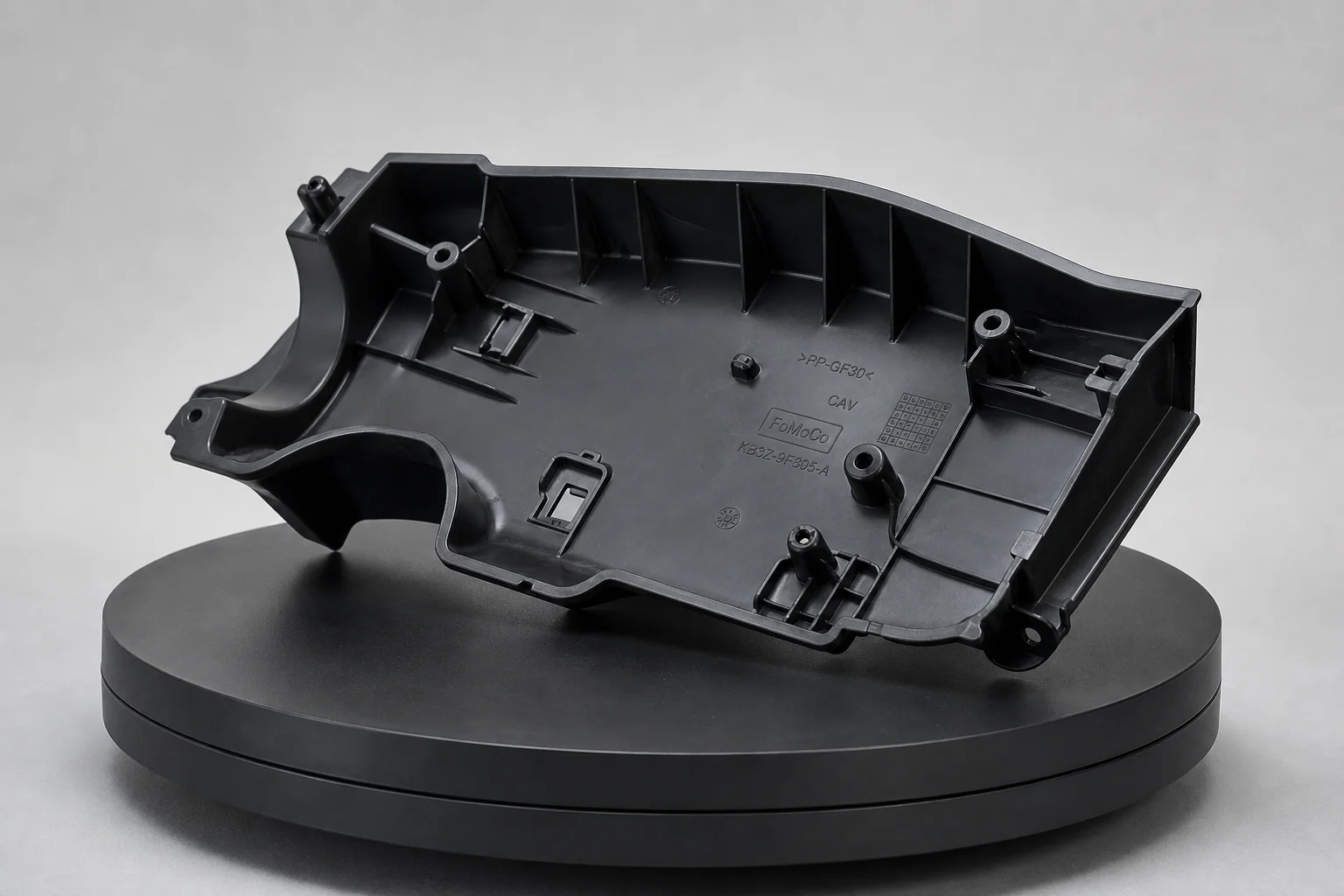 Black automotive plastic part with deep pockets and embossed text on turntable