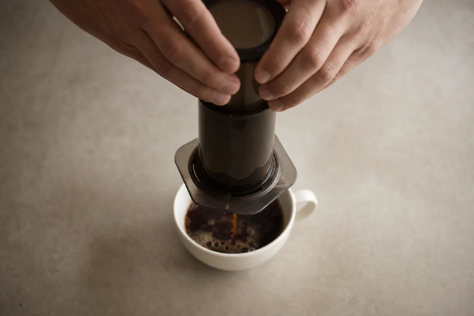 Hands pressing AeroPress with coffee flowing into cup below