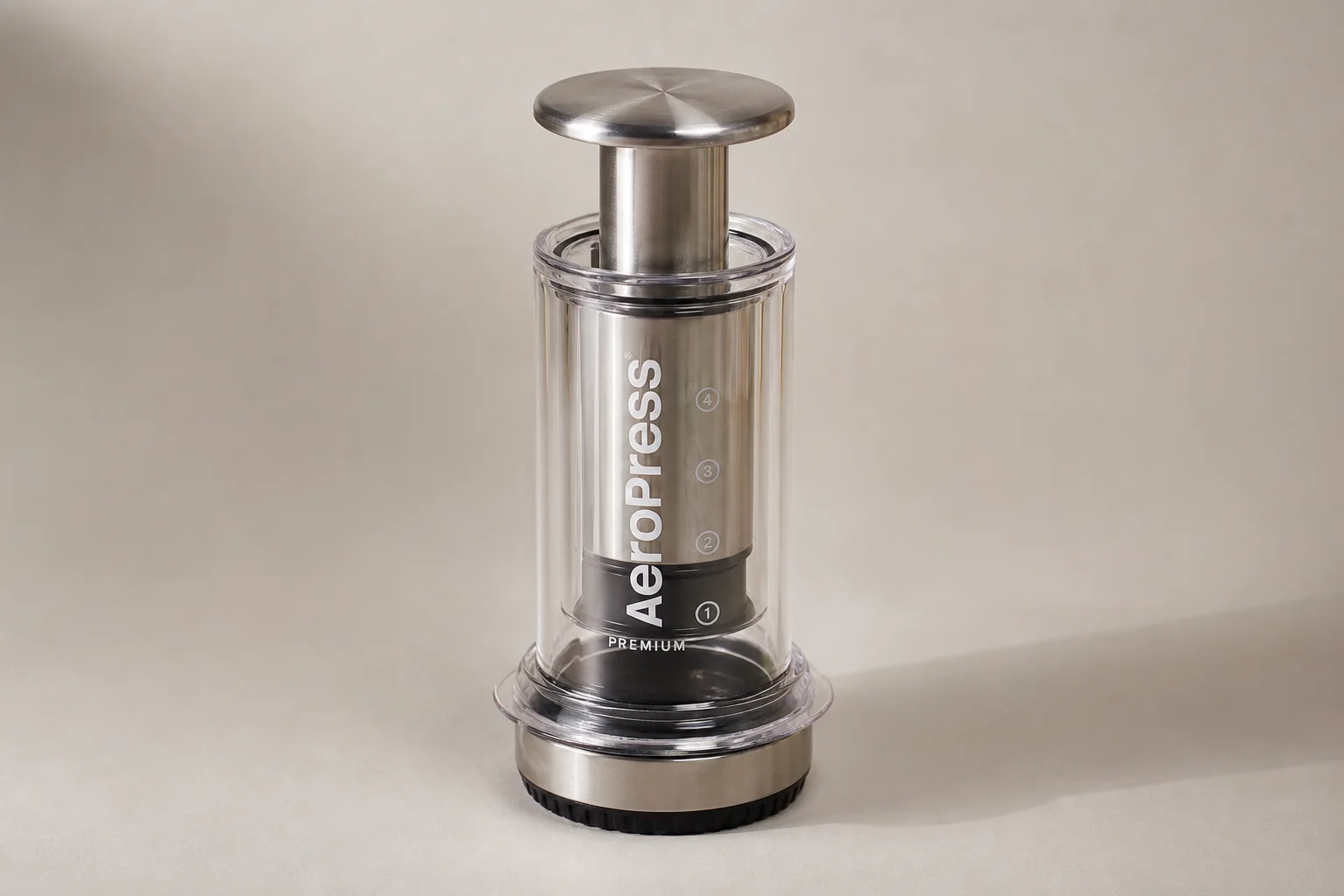AeroPress Premium brewer with glass chamber, stainless steel cap, and aluminum plunger on neutral background
