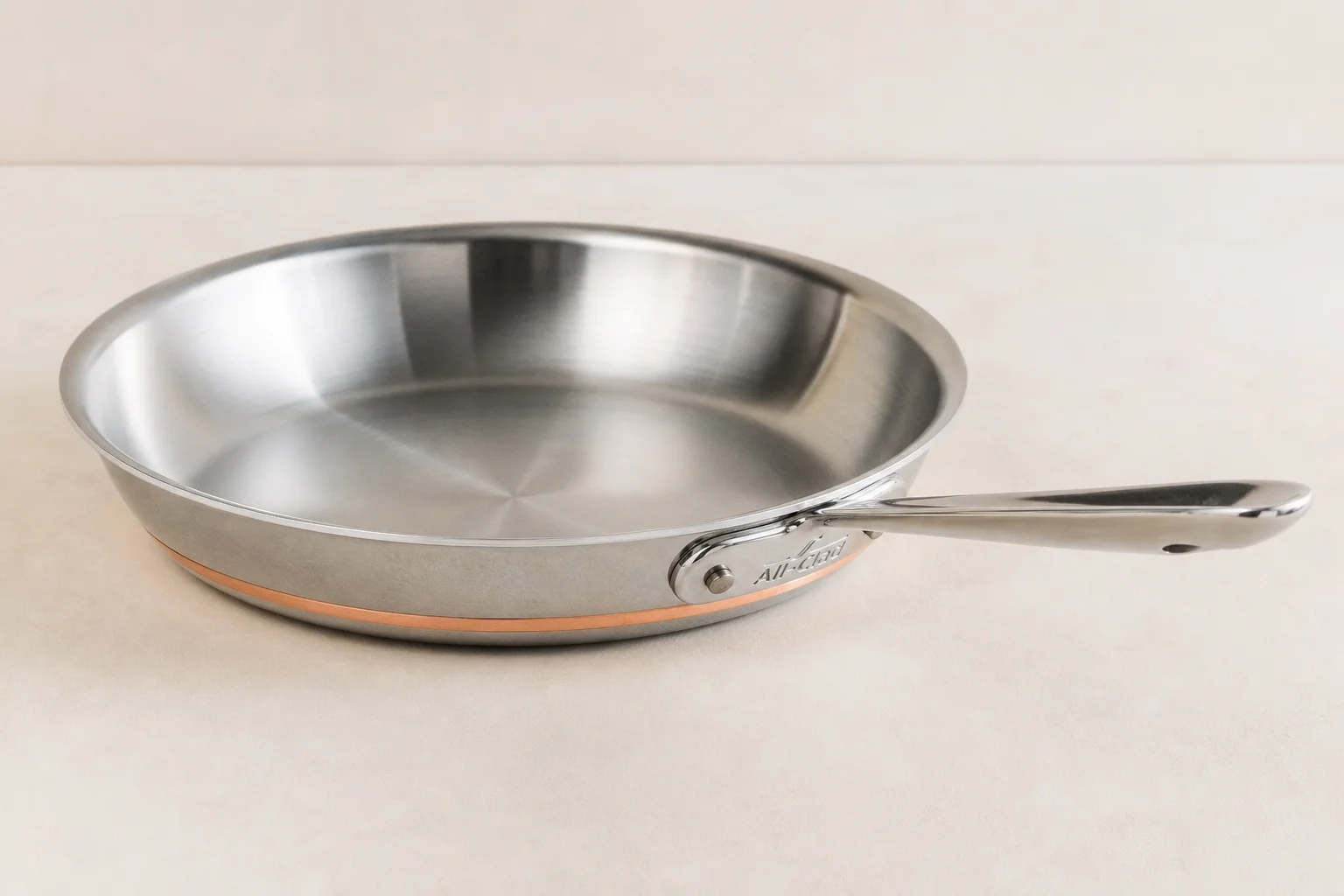 Collection of six stainless steel frying pans with varied finishes and handle styles on concrete surface