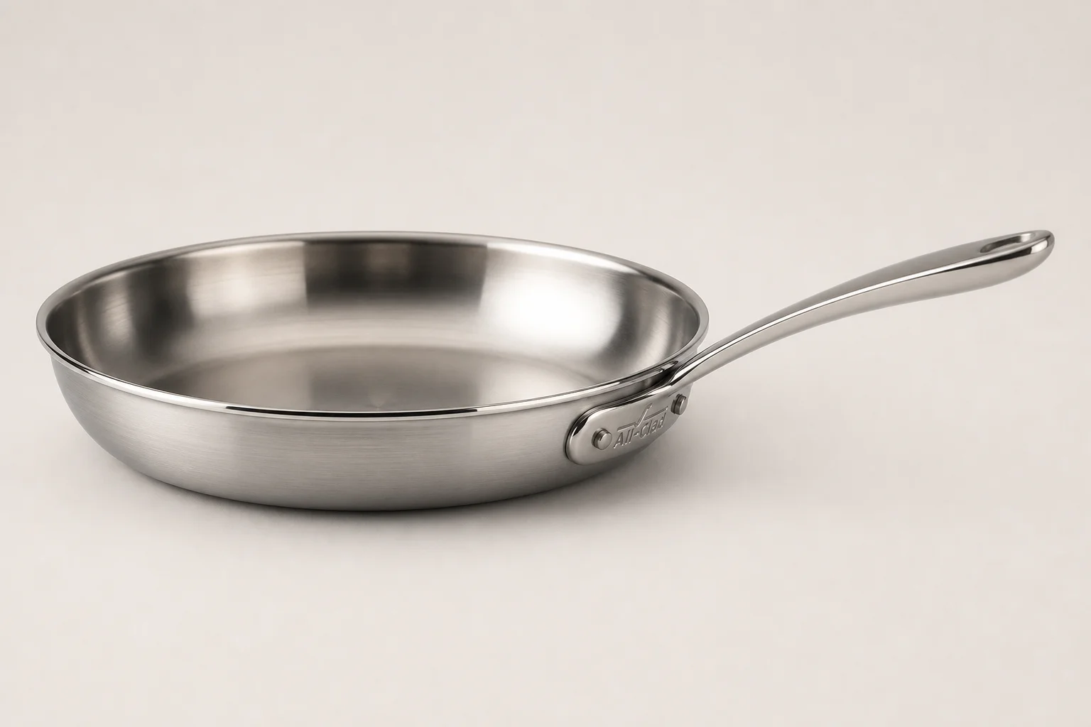Collection of six stainless steel frying pans with varied finishes and handle styles on concrete surface