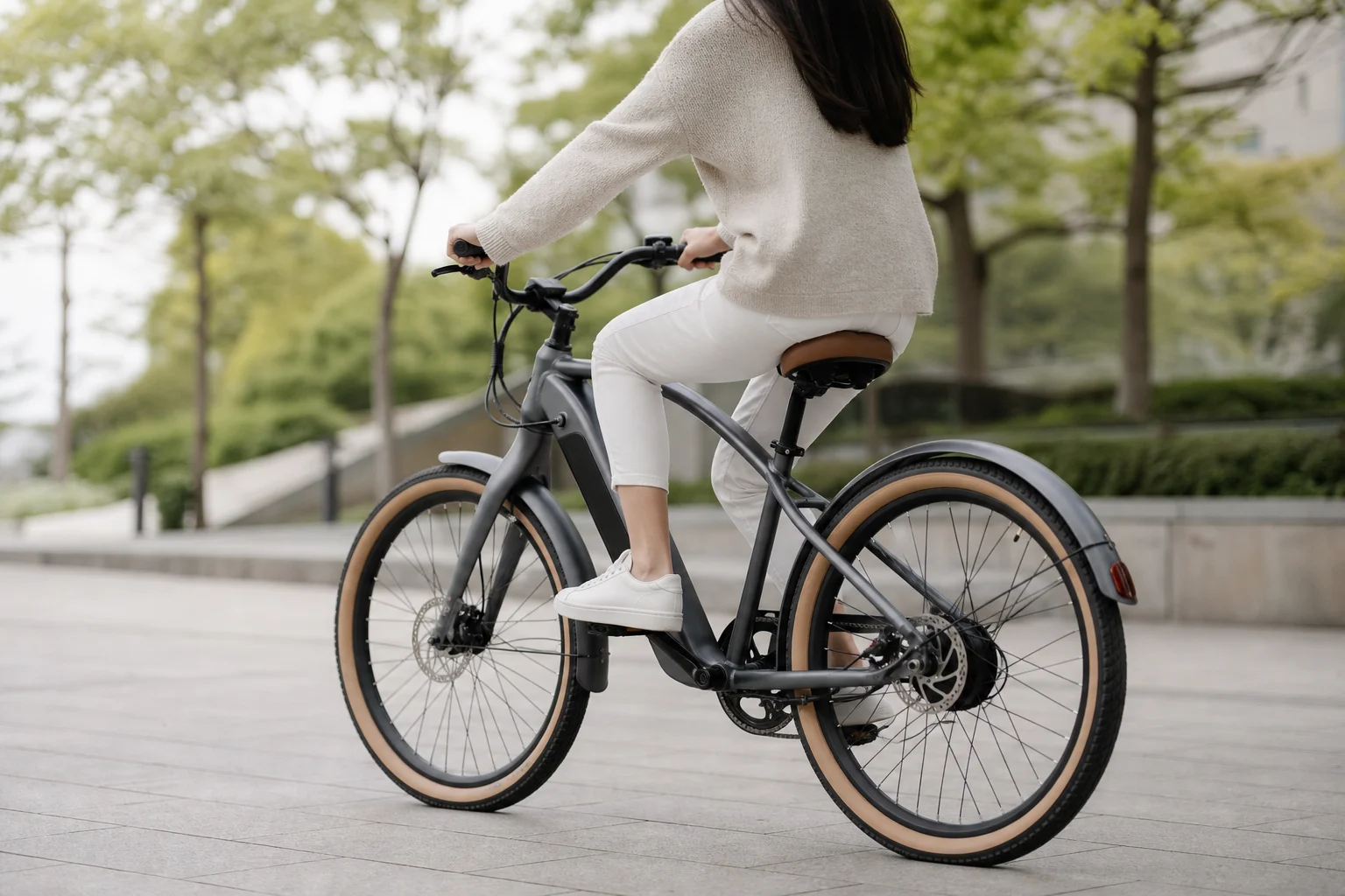 Cyclist riding cruiser e-bike on smooth urban path with trees in background