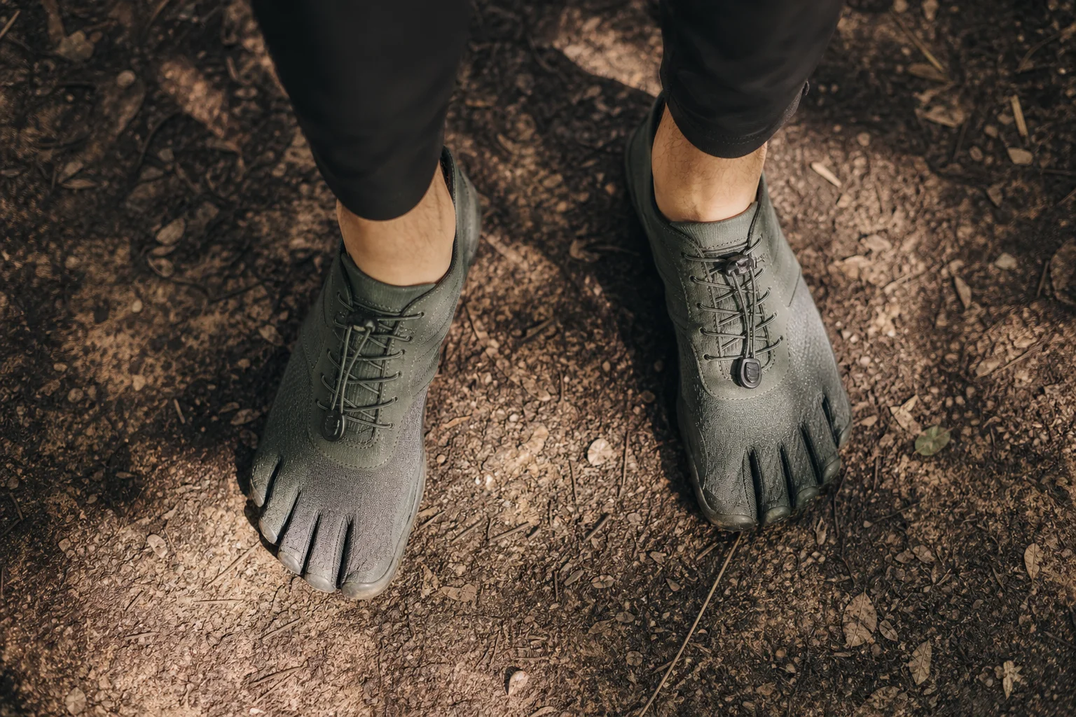 Runner's feet in barefoot shoes on natural trail surface with dappled sunlight
