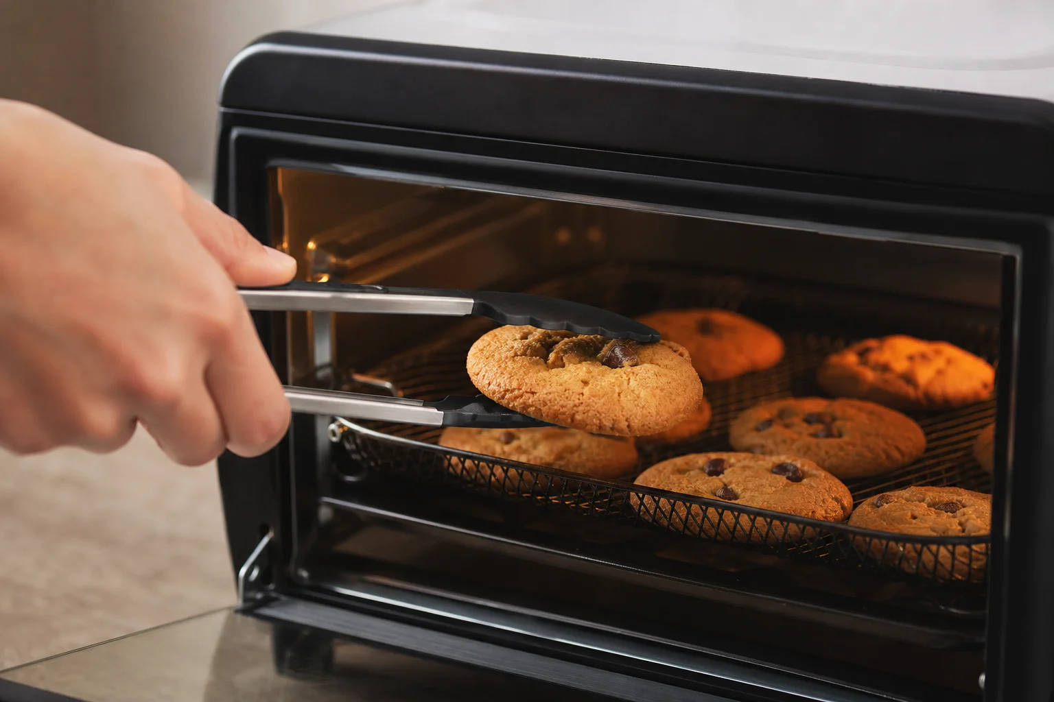 Hands removing a baked cookie from an air fryer toaster oven