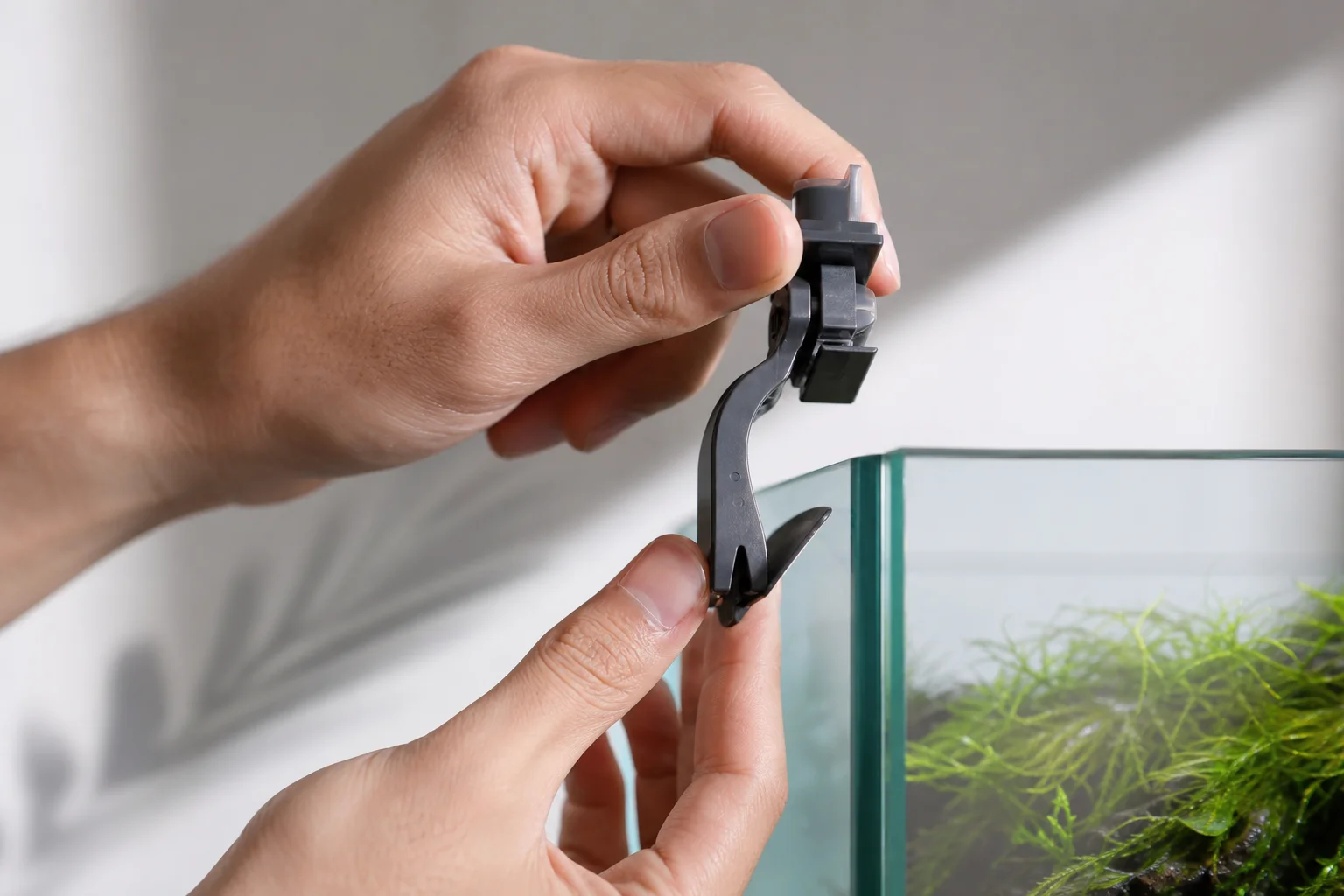 Hands adjusting feeder bracket on aquarium glass edge