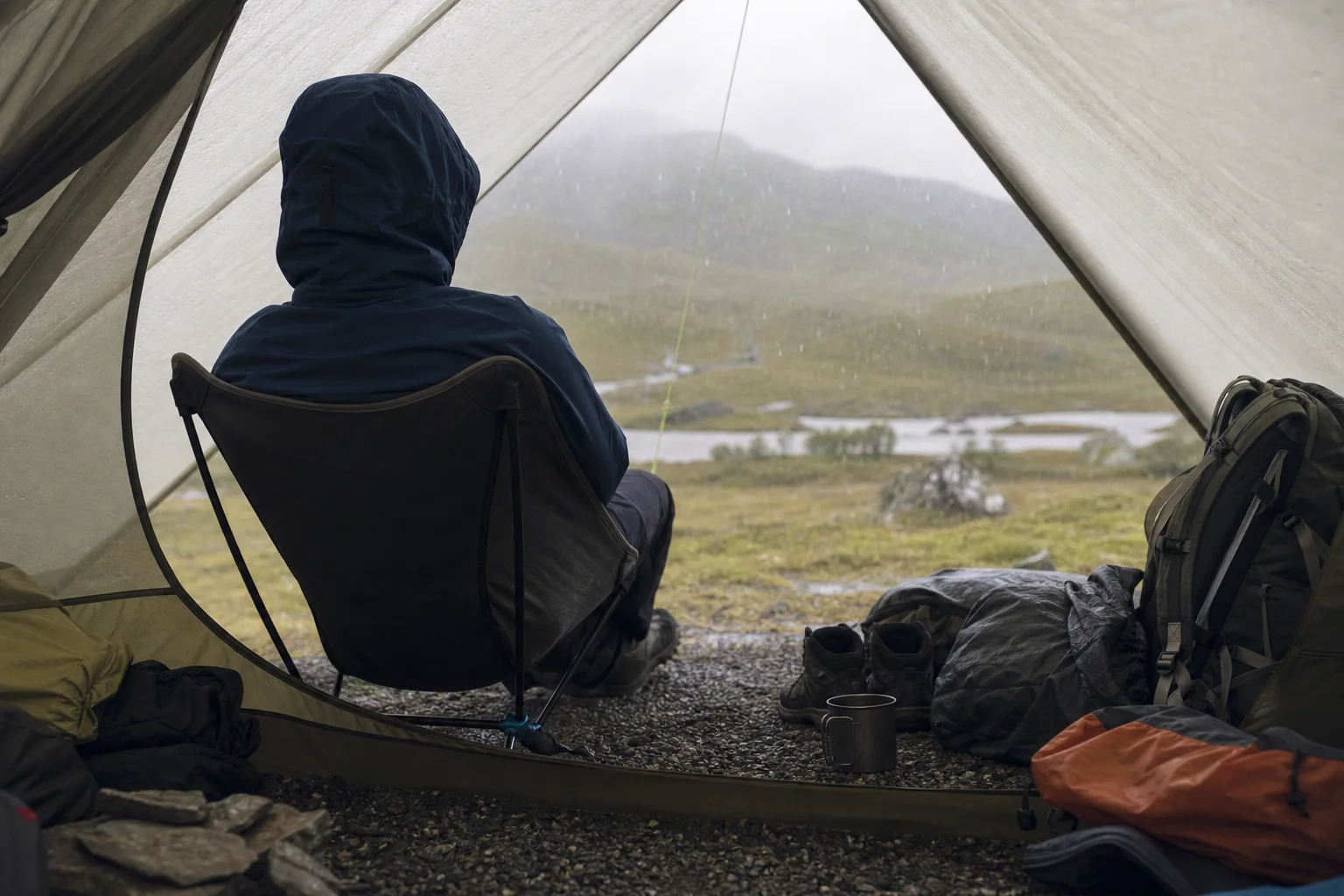 Backpacker in ground chair inside tent shelter during rain