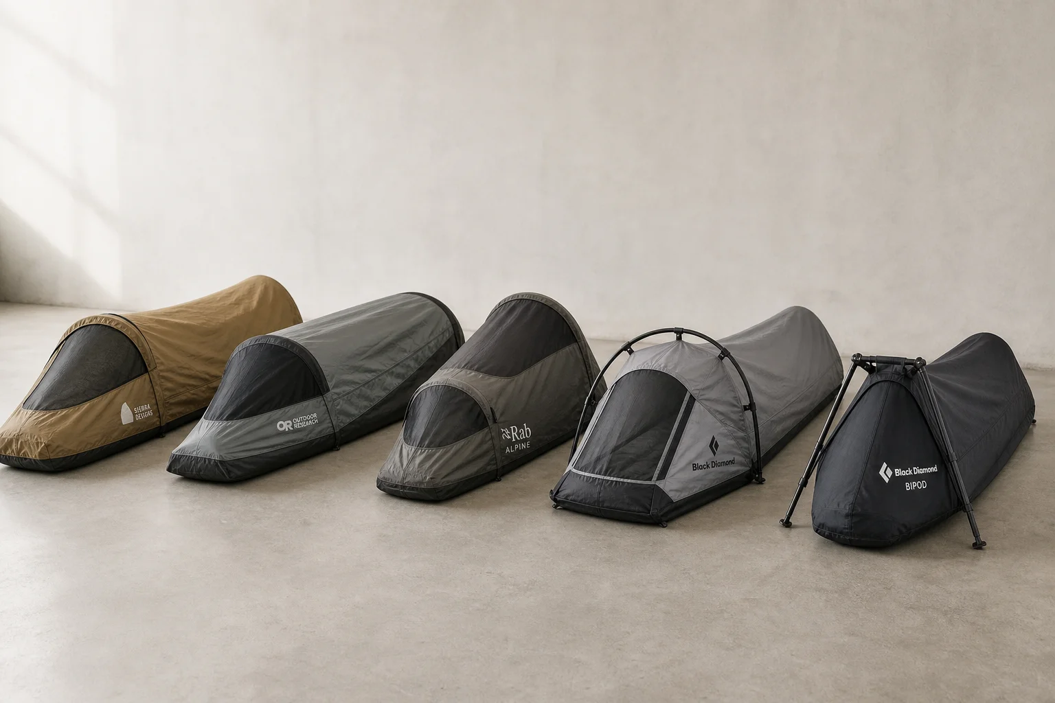 Five bivvy bags displayed in a row on concrete surface showing different designs and colors