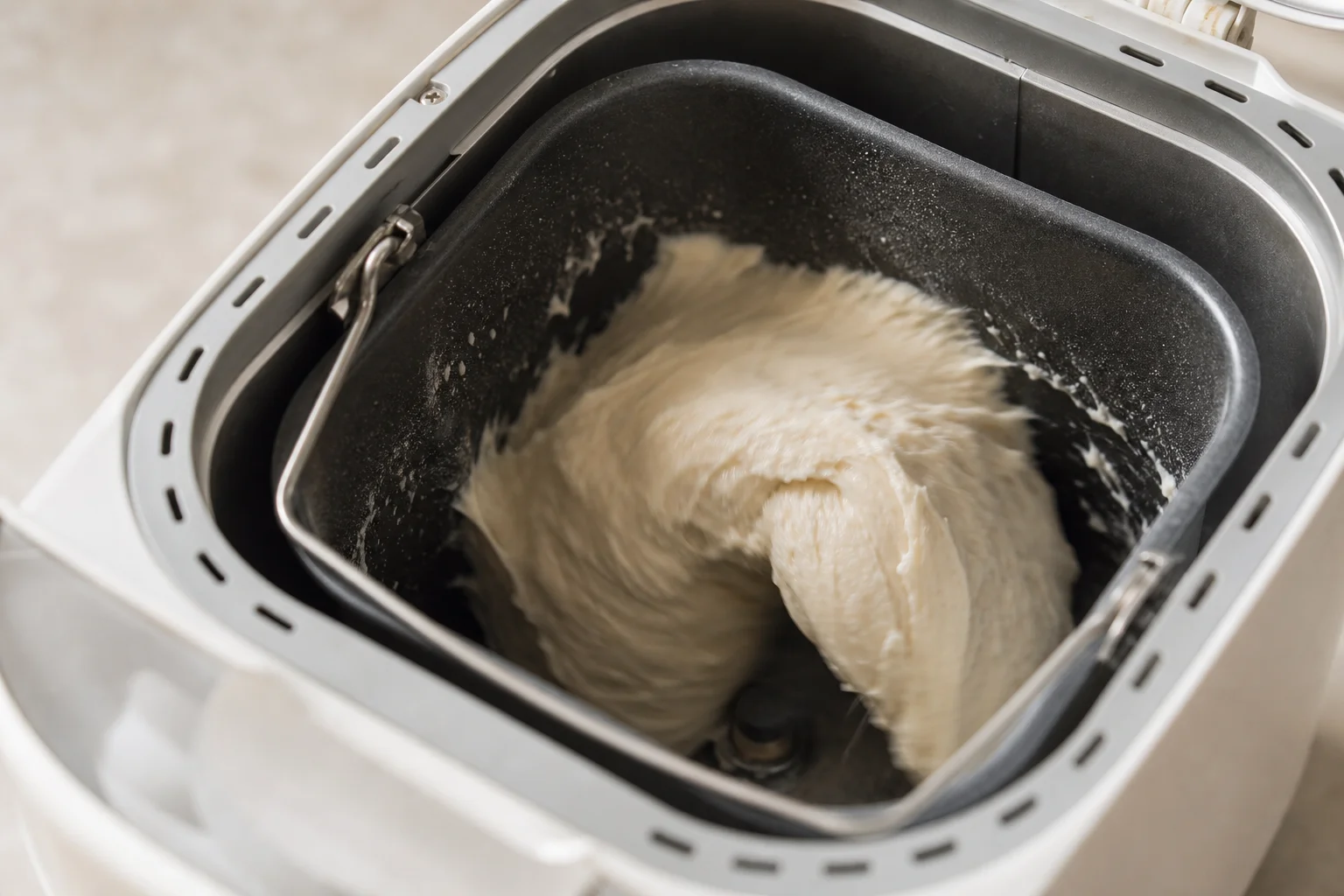 Hands kneading dough in a bread maker with visible mixing action