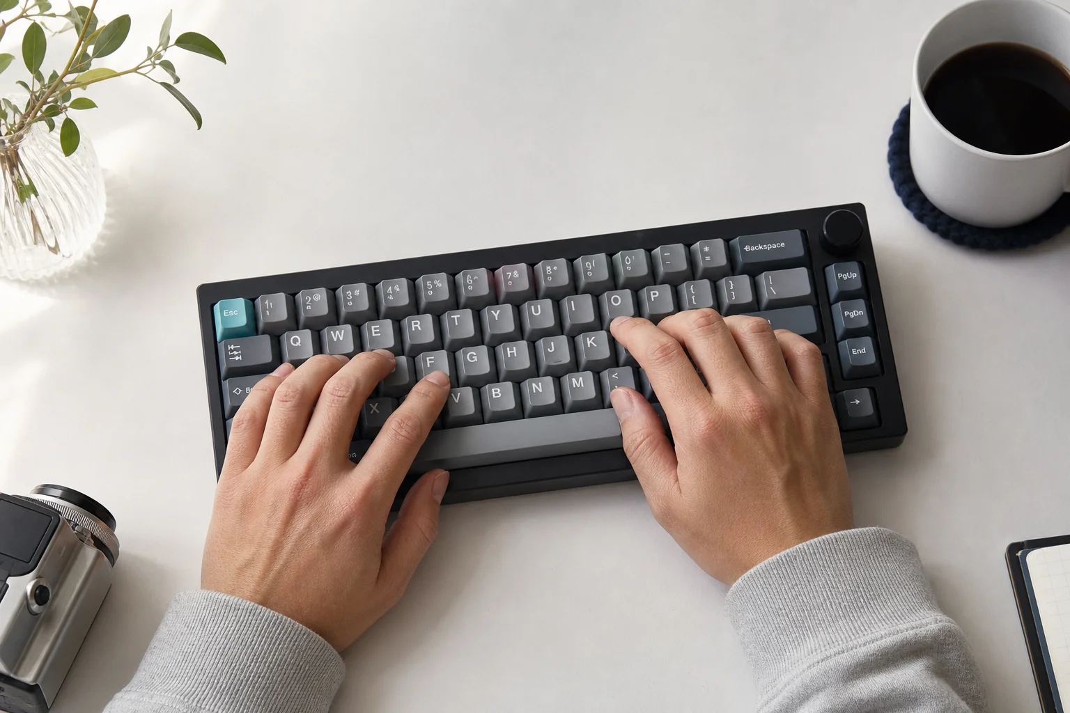 Hands typing on a compact mechanical keyboard at a minimalist desk