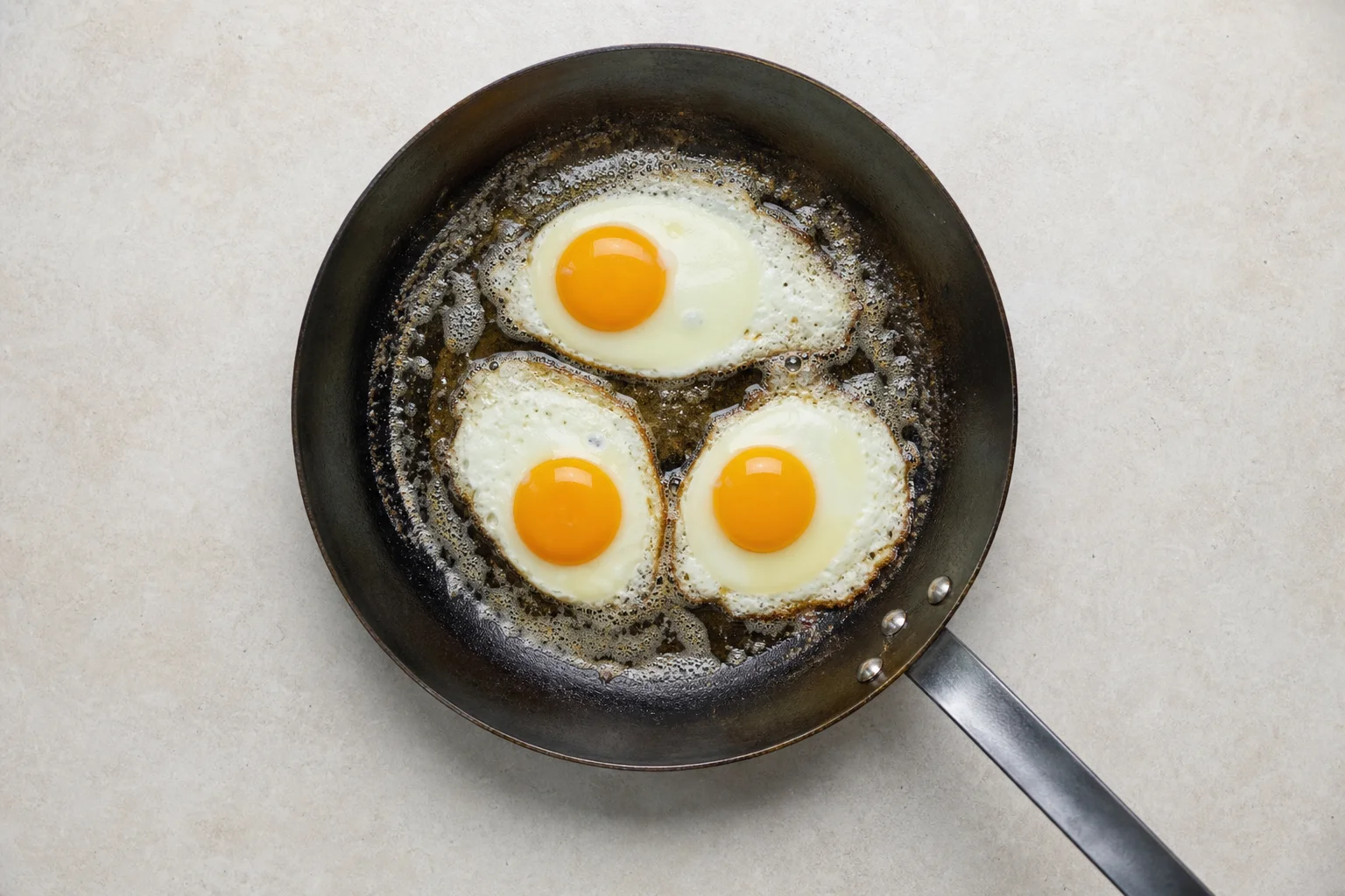 Overhead view of eggs cooking evenly across a carbon steel pan surface