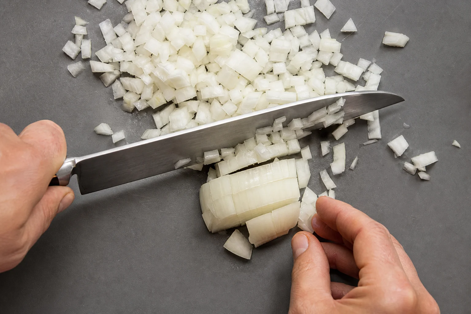 Chef's knife dicing onions into uniform pieces on a cutting board