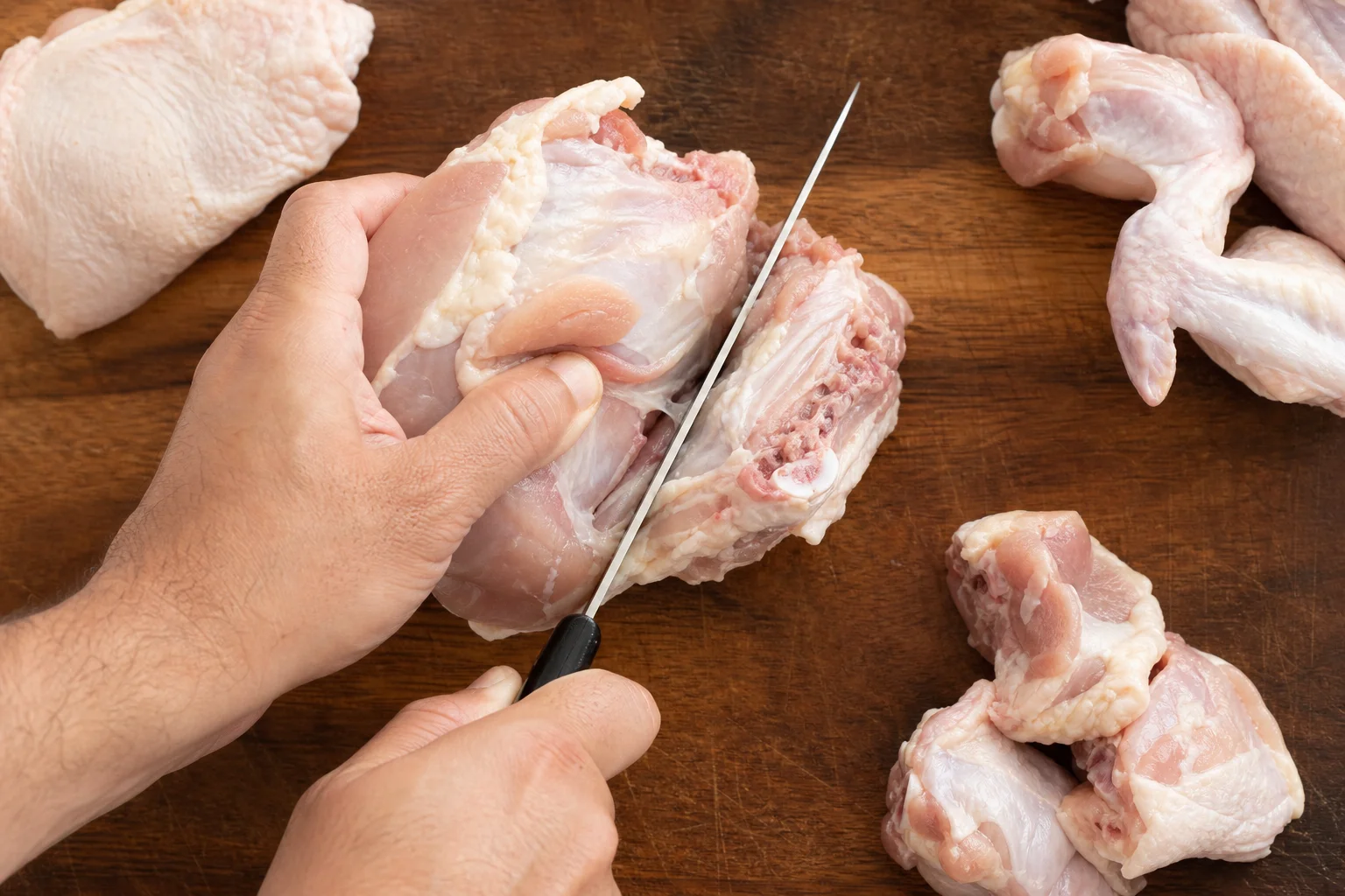 Chef's knife cutting through raw chicken on a cutting board