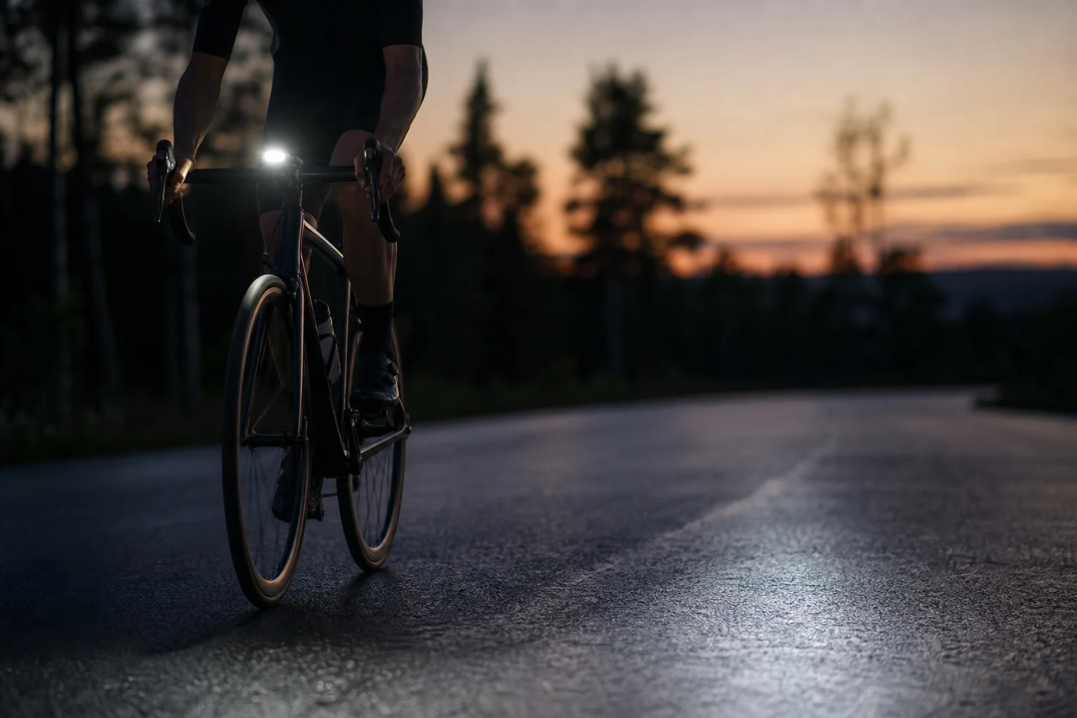 A road cyclist riding at night, with a bike light illuminating the road ahead