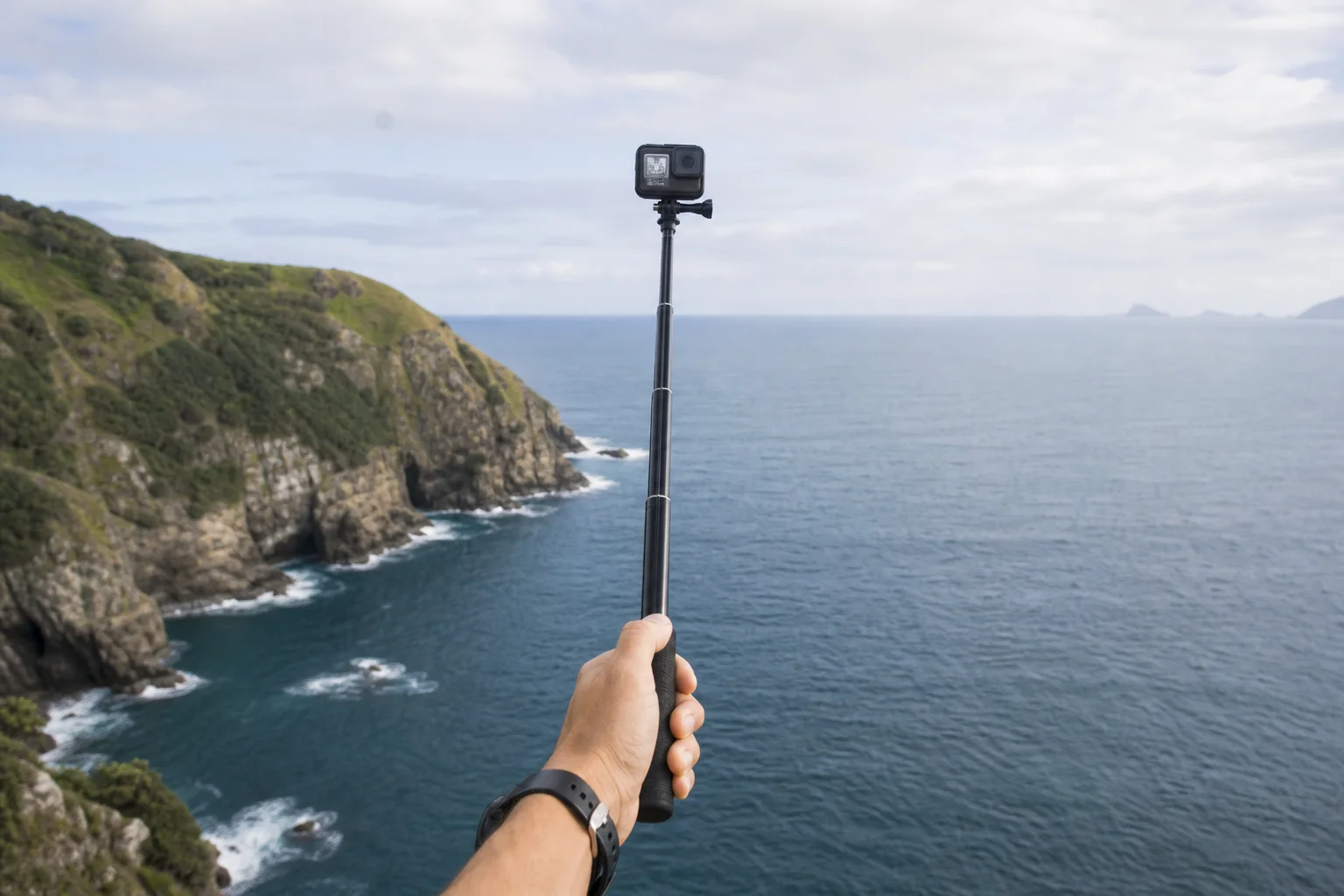 Extended GoPro pole capturing scenic coastal landscape with cliffs