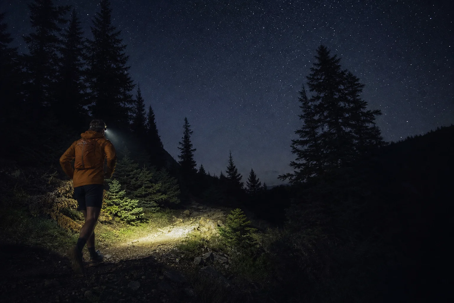 Trail runner wearing head torch on dark forest path at night