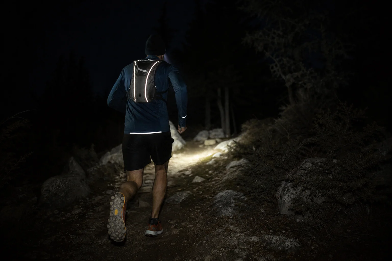 Night runner in motion wearing lightweight headlamp on dark trail