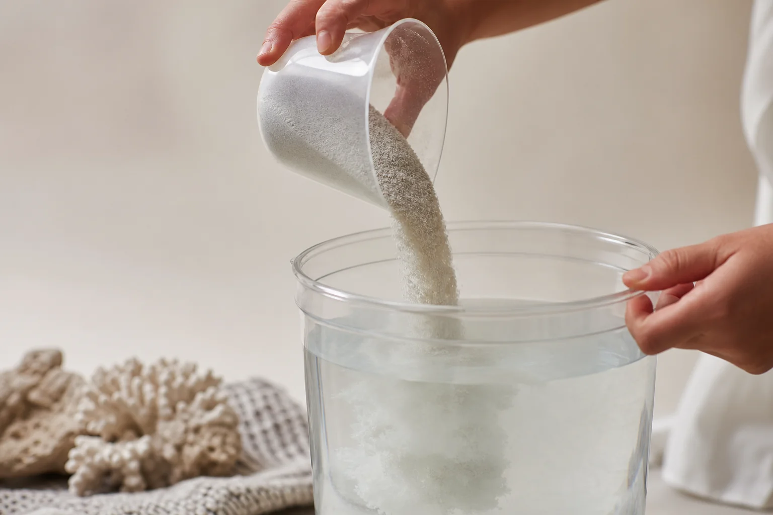 Hands pouring dry saltwater mix powder into bucket of water