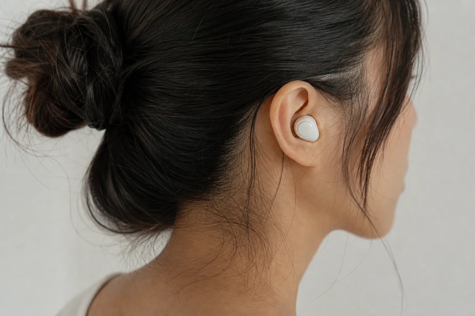 Person wearing earbuds in listening environment with neutral backdrop