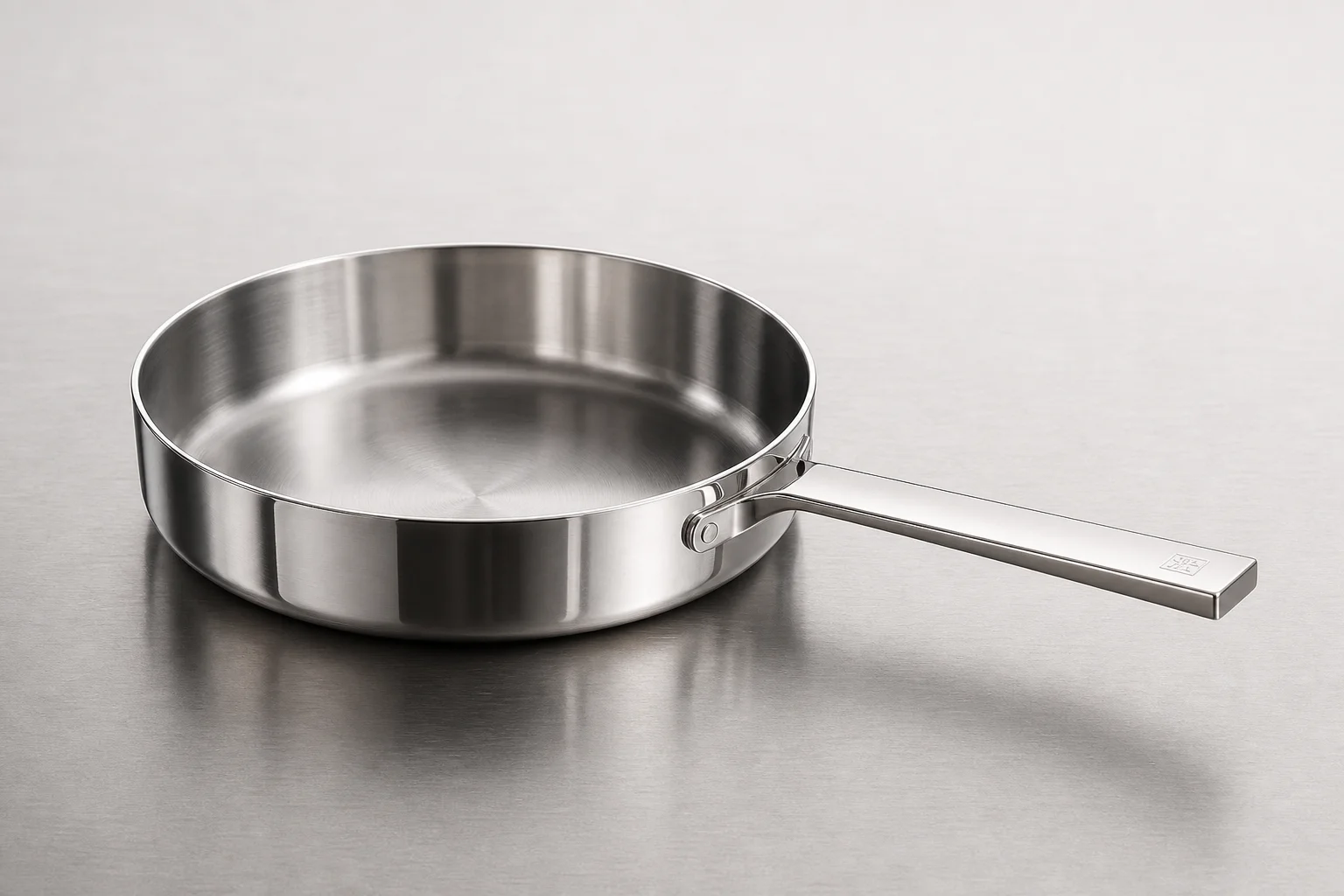 Collection of six stainless steel frying pans with varied finishes and handle styles on concrete surface