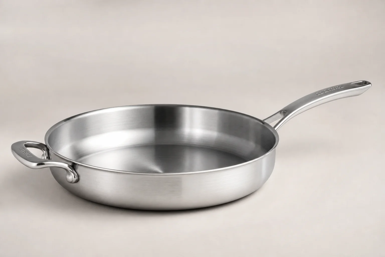 Collection of six stainless steel frying pans with varied finishes and handle styles on concrete surface