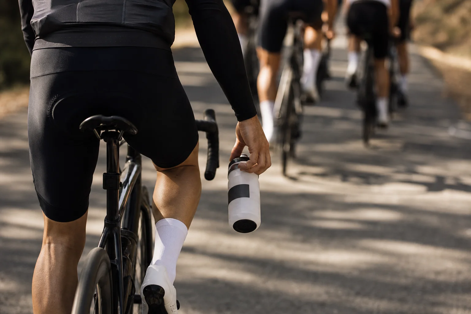 Cyclist holding a water bottle during a group ride on a sunny road