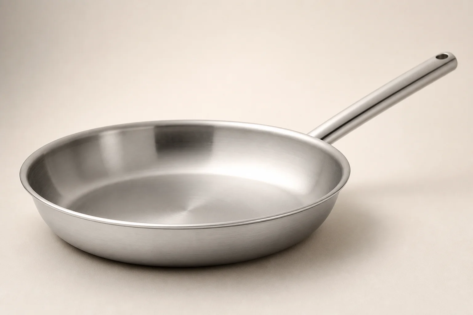 Collection of six stainless steel frying pans with varied finishes and handle styles on concrete surface