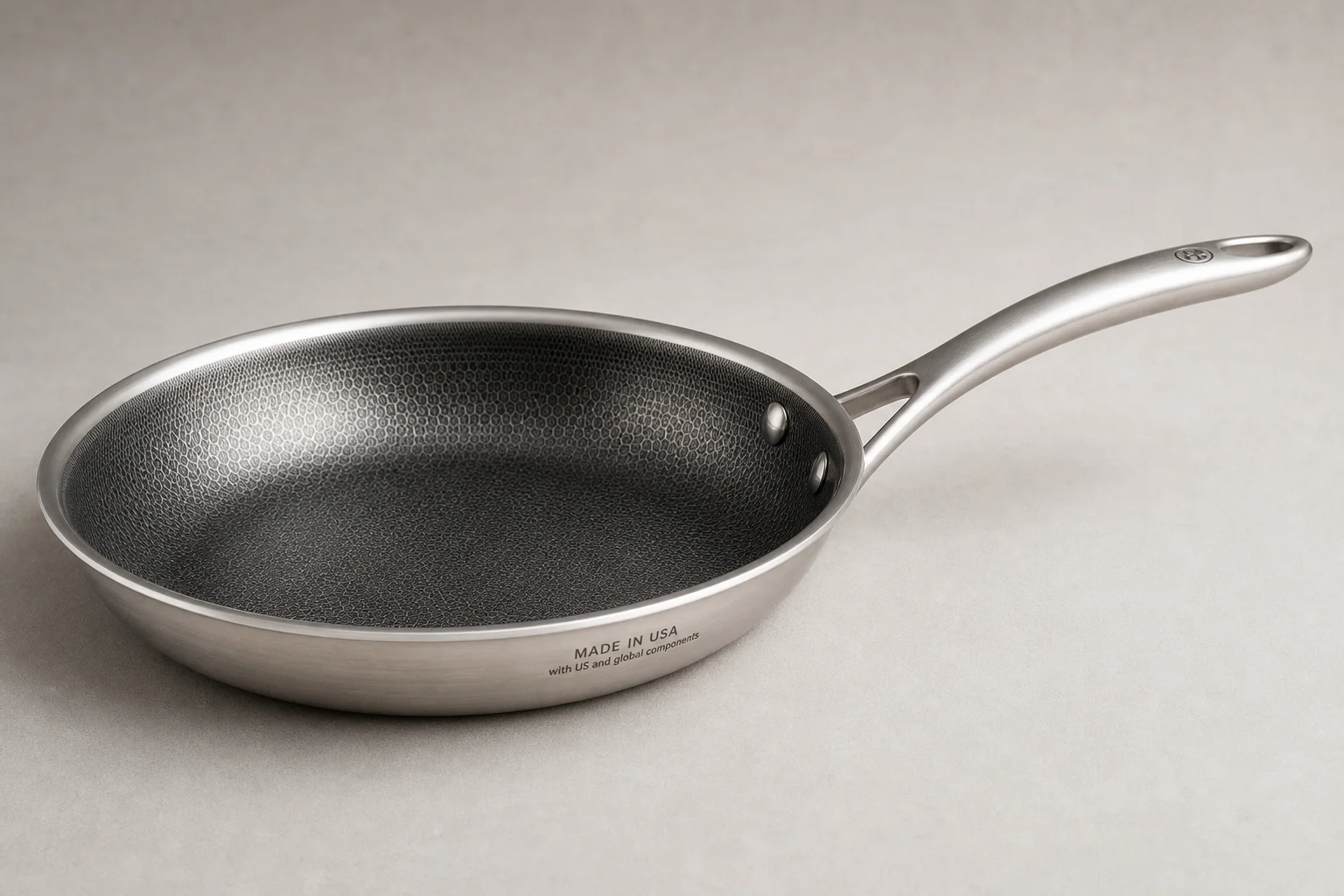 Collection of six stainless steel frying pans with varied finishes and handle styles on concrete surface