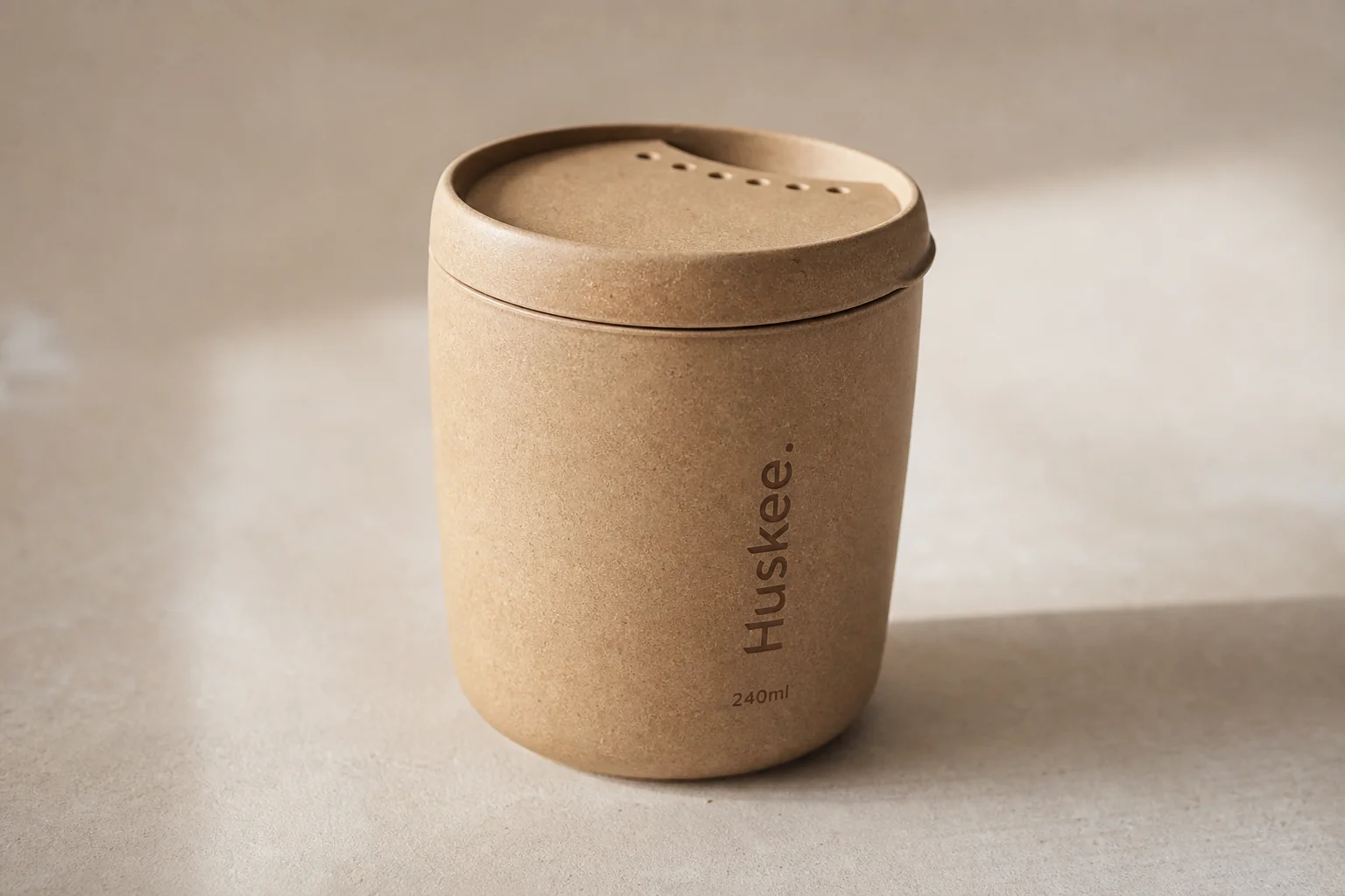 Eight reusable coffee cups arranged on concrete surface showing variety of materials and designs