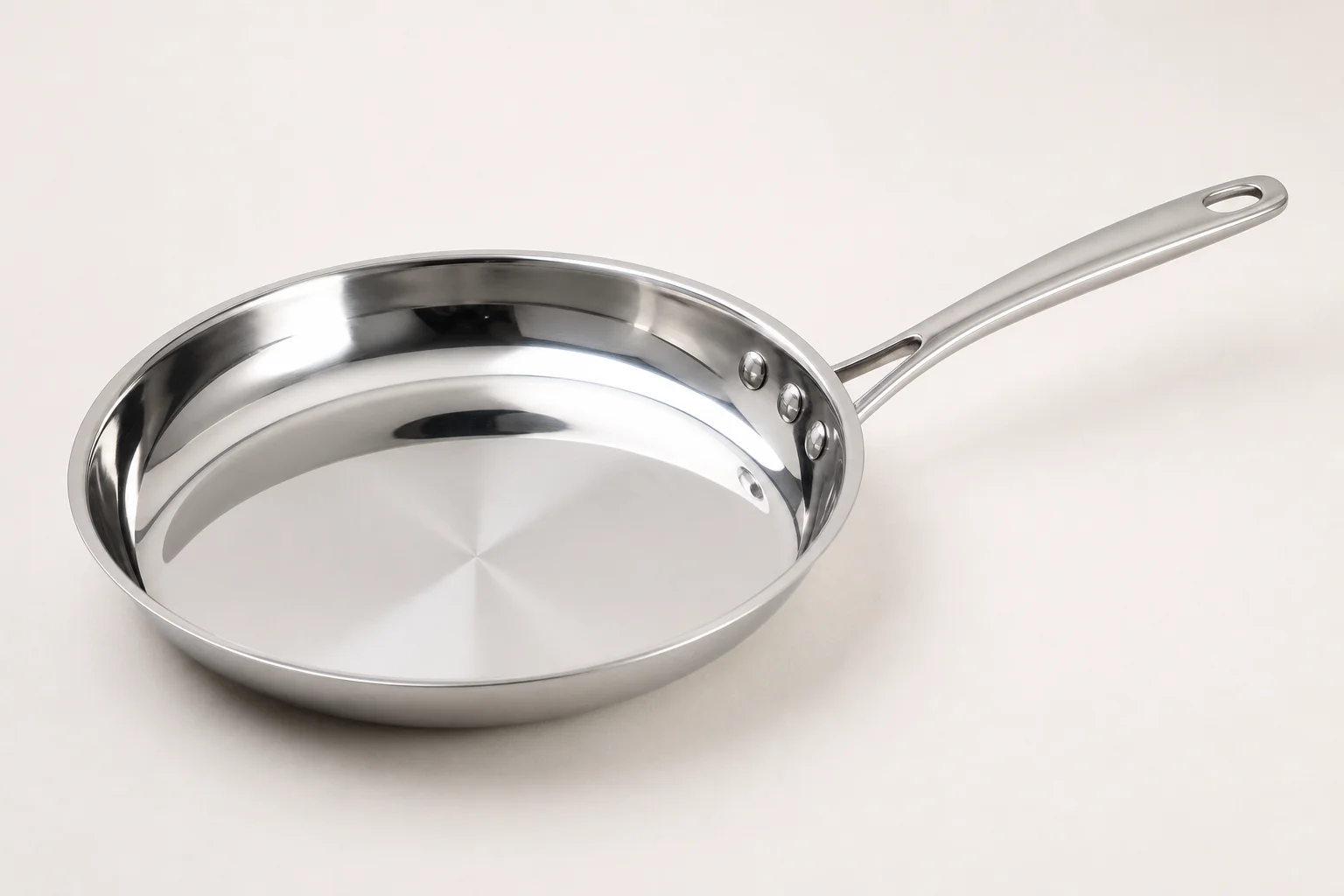 Collection of six stainless steel frying pans with varied finishes and handle styles on concrete surface