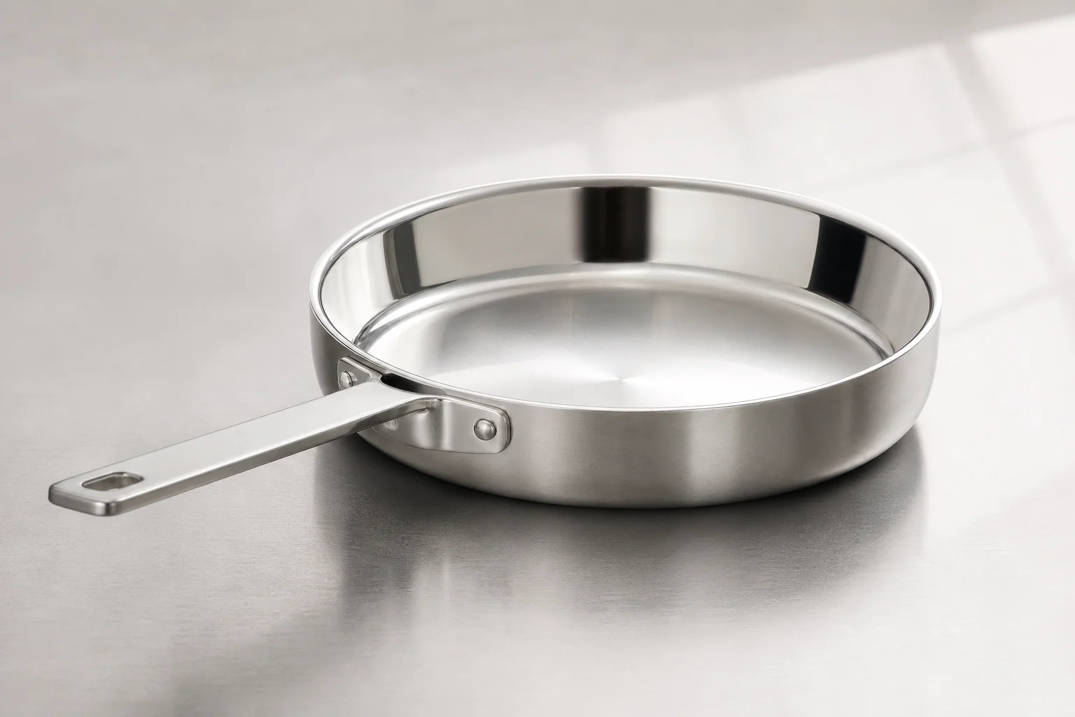 Collection of six stainless steel frying pans with varied finishes and handle styles on concrete surface