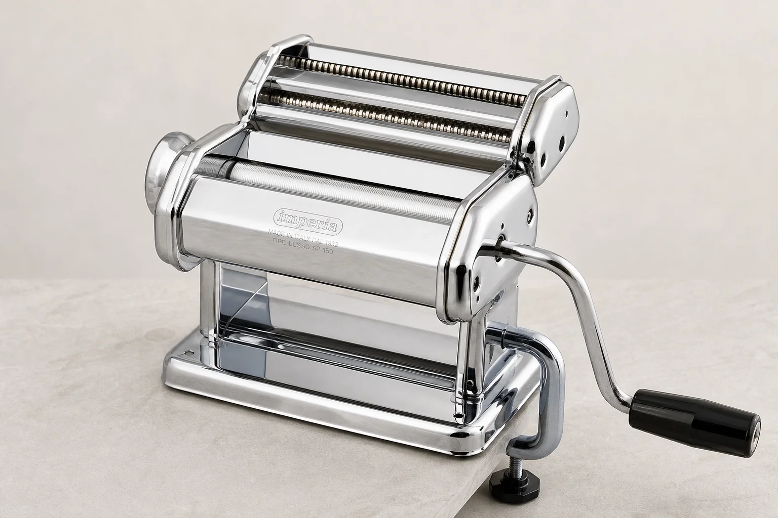 Five pasta makers arranged on wood surface including hand-crank and powered models