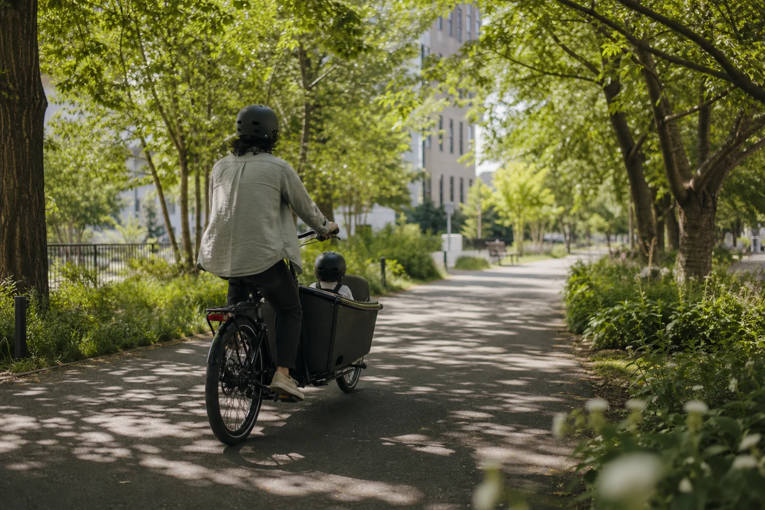 Parent and child riding a cargo bike on a tree-lined urban path
