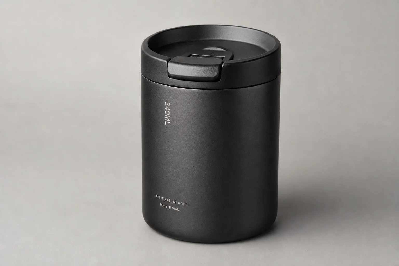 Eight reusable coffee cups arranged on concrete surface showing variety of materials and designs