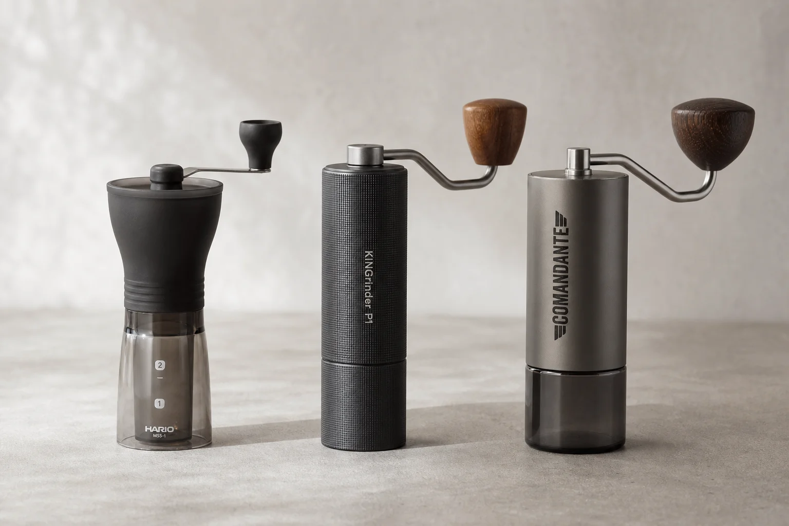 三款手搖磨豆機：Hario Slim、KINGrinder P1 與 Comandante 擺放在水泥地上