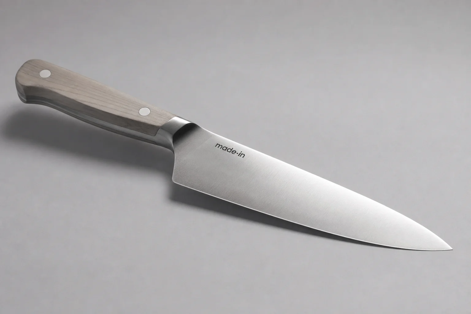 Four chef's knives arranged diagonally on concrete: Misen, Made-In, Victorinox, and Shun
