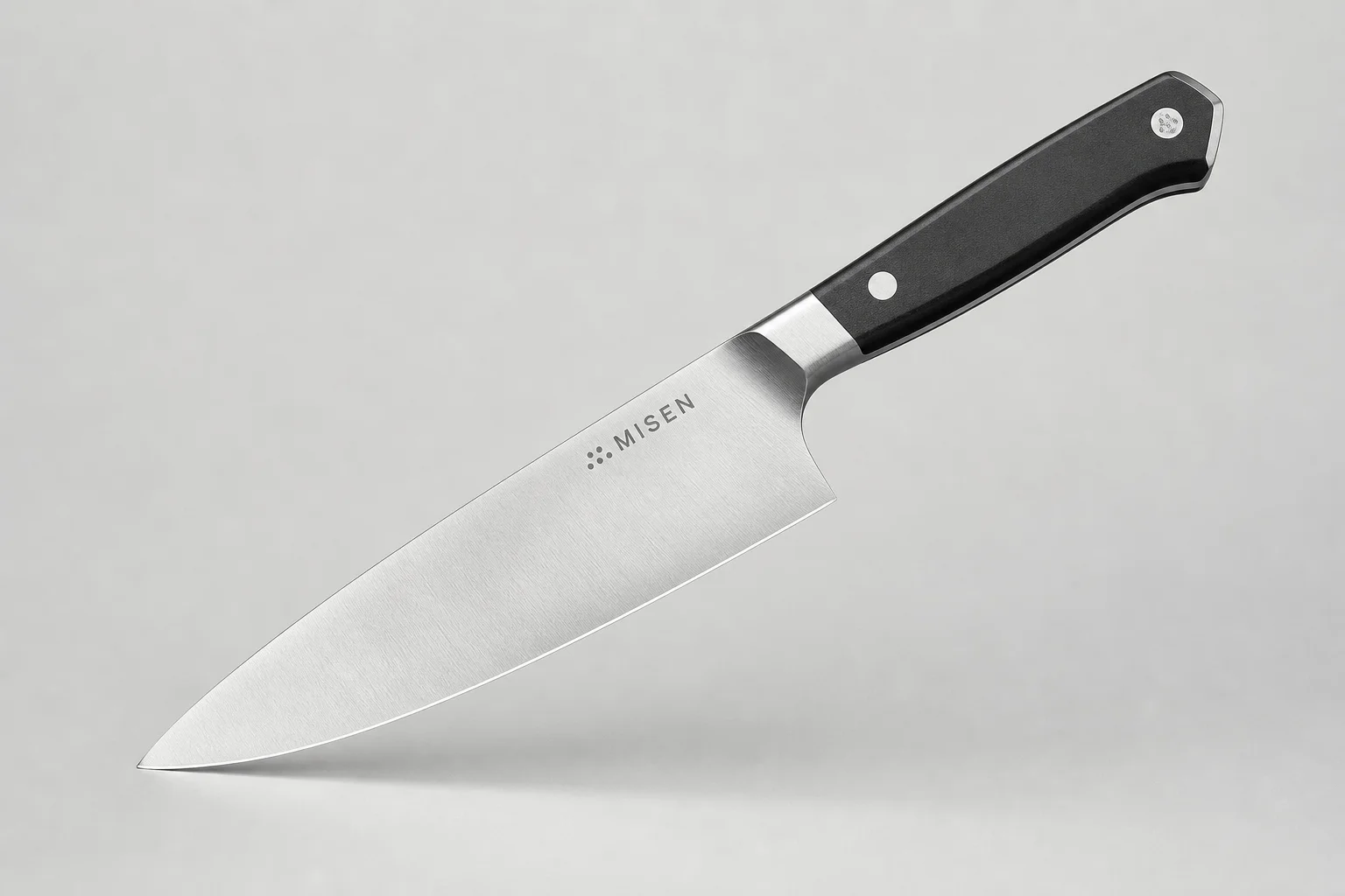 Four chef's knives arranged diagonally on concrete: Misen, Made-In, Victorinox, and Shun