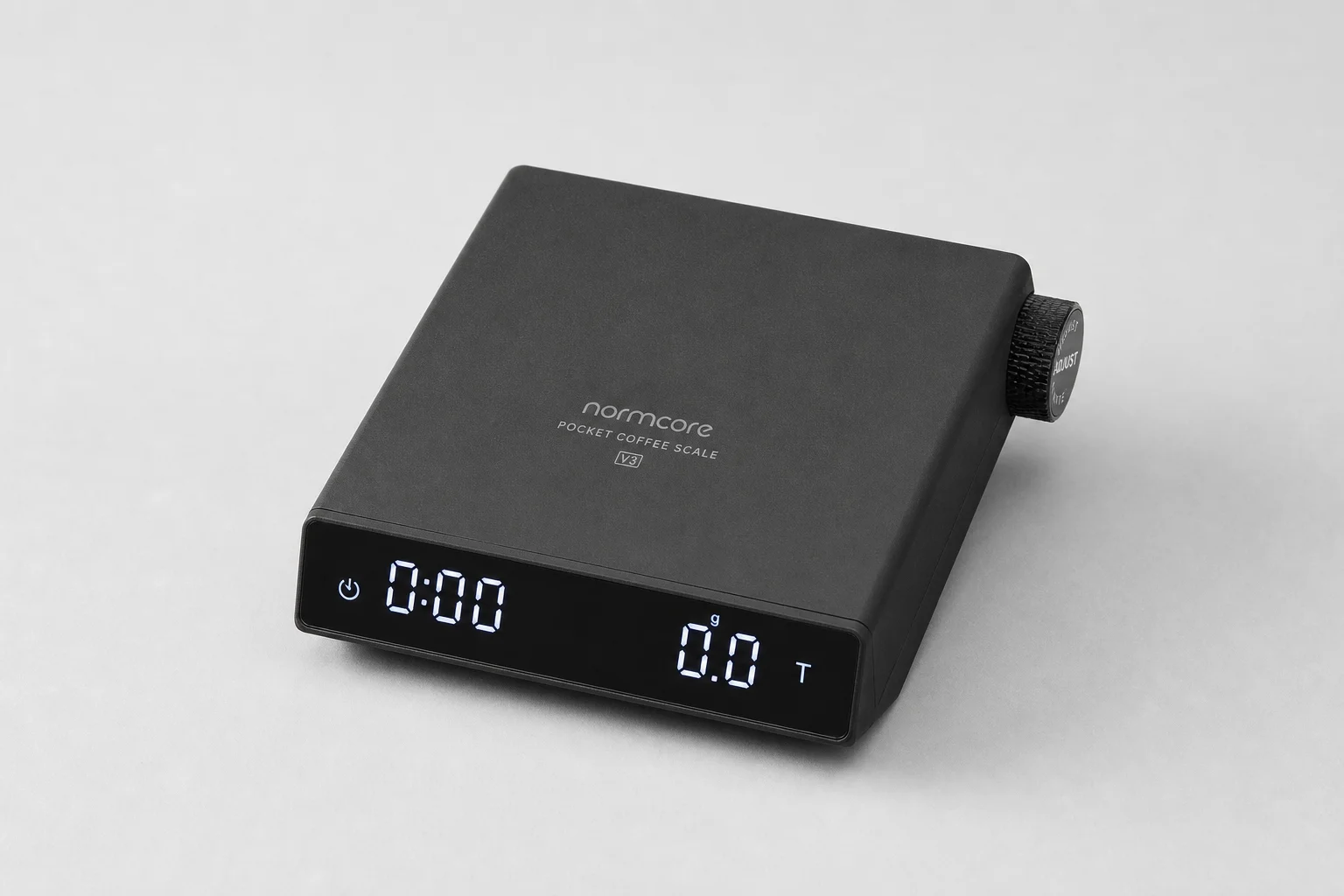 Normcore Pocket Coffee Scale V3 放置於灰色背景上，展示其輕巧的鋁合金設計與數位顯示螢幕