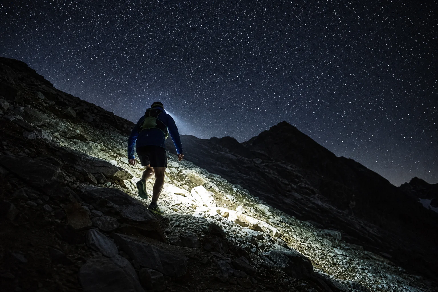 Trail runner ascending a steep mountain slope at night with headlamp beam visible