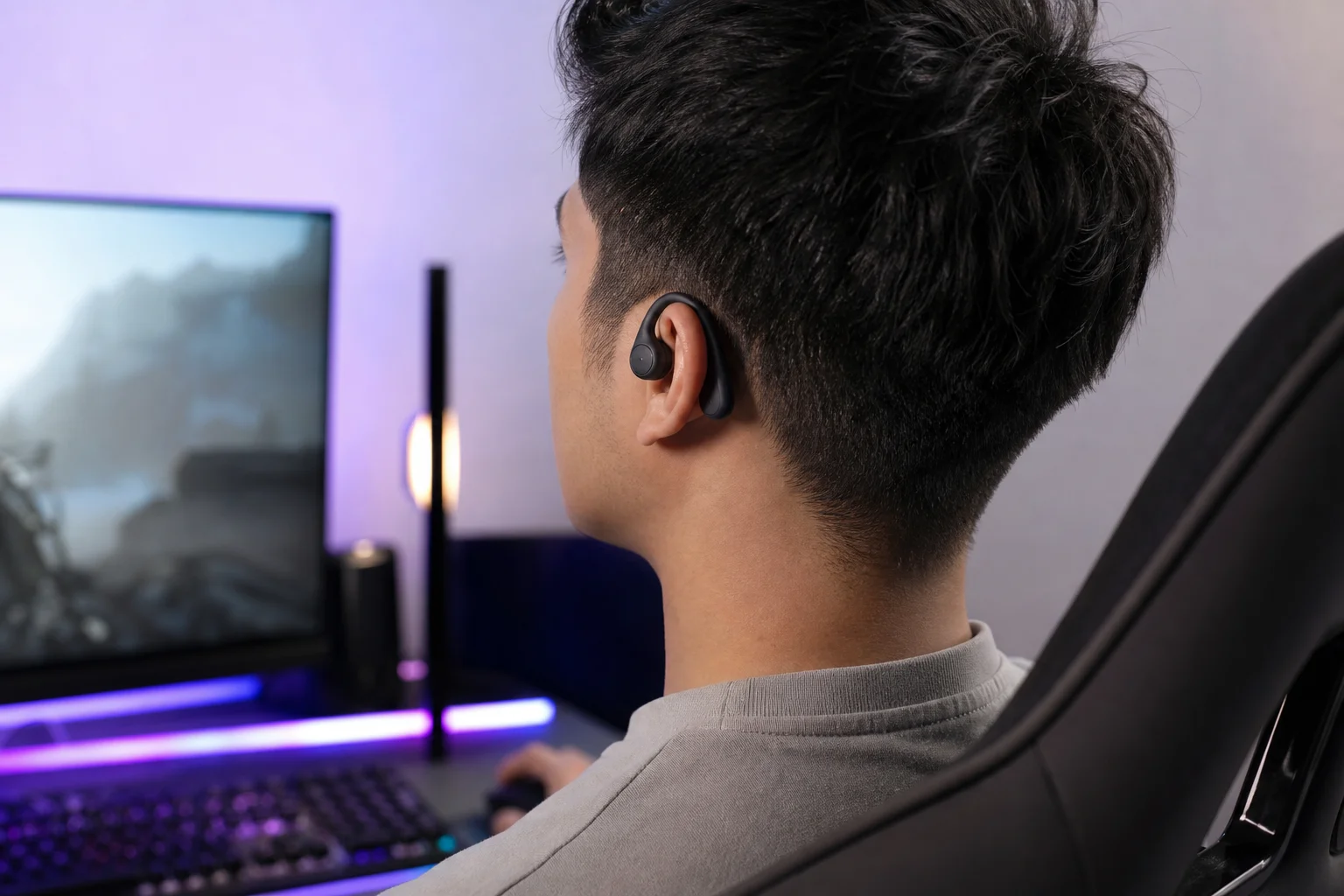 Gamer wearing open-back earbuds at a gaming desk with RGB lighting