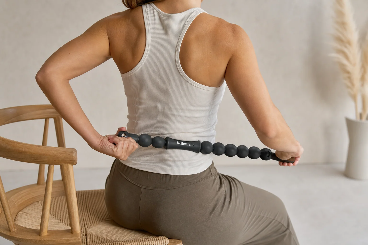 Person seated demonstrating mid-back and lower-back massage technique with Roller Cane