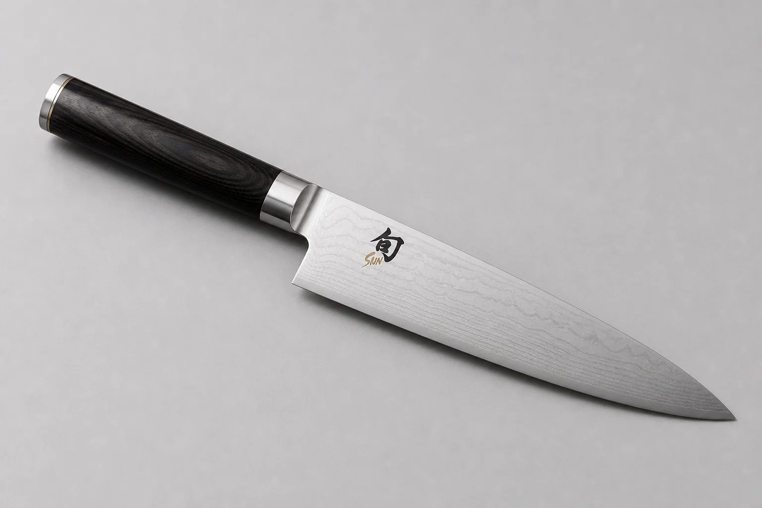 Four chef's knives arranged diagonally on concrete: Misen, Made-In, Victorinox, and Shun